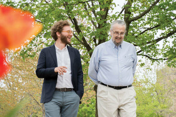 Professors Nuno Moniz and Don Howard walk on campus in the spring, talking together.