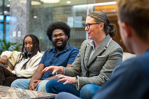 Teacher on sofa talking with three students in library setting