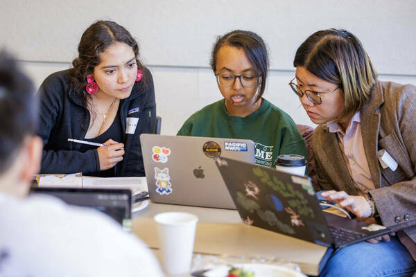 Three women work on computers collaboratively.