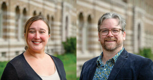 Two individuals smile in front of a Collegiate Gothic-style building. On the left, a woman with light brown hair wears a black cardigan. On the right, a man with graying hair, glasses, and a beard wears a dark blue corduroy blazer over a floral patterned shirt.