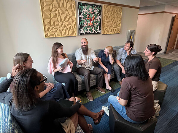 A diverse group of eight people sits in a circle, discussing.