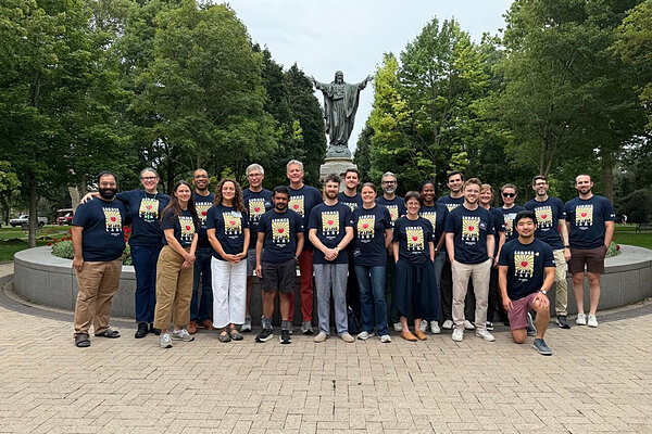 Group of people in dark blue "Summer of Love Camp" t-shirts posing before a statue of Jesus.